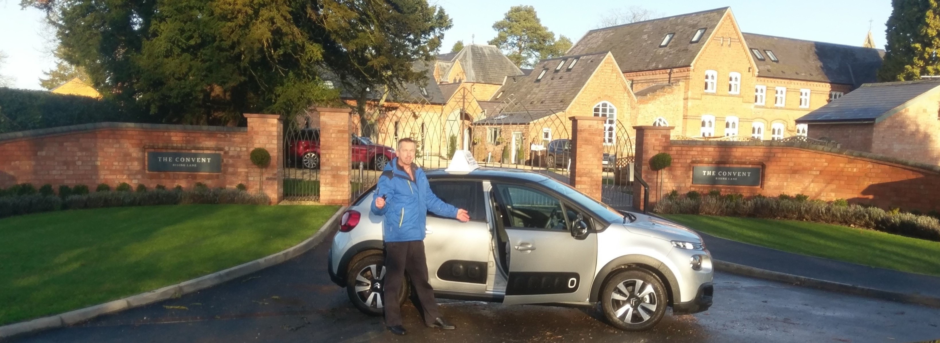 Tim Walsh welcoming you to enter his instructor car, standing in front of The Convent, Rising Lane apartments